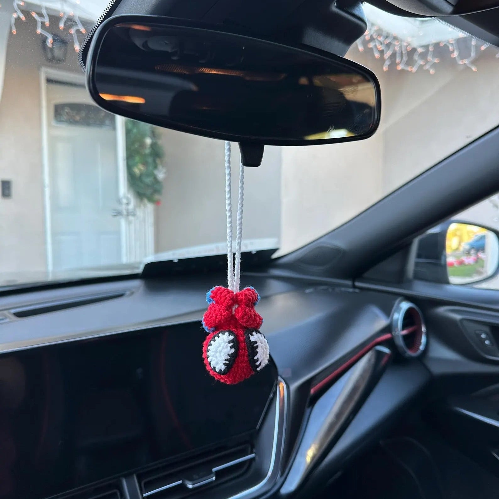 Car interior with a red and white hanging ornament near the rearview mirror.