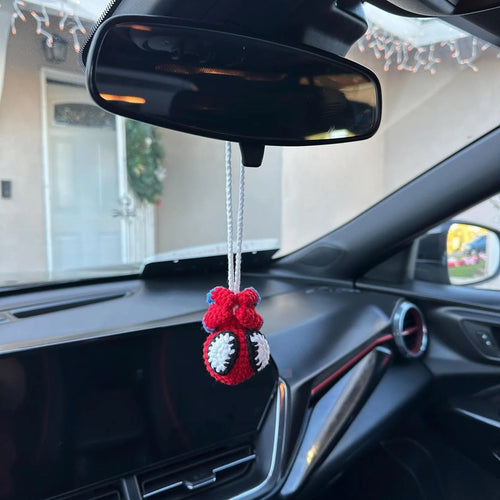 Car interior with a red and white hanging ornament near the rearview mirror.