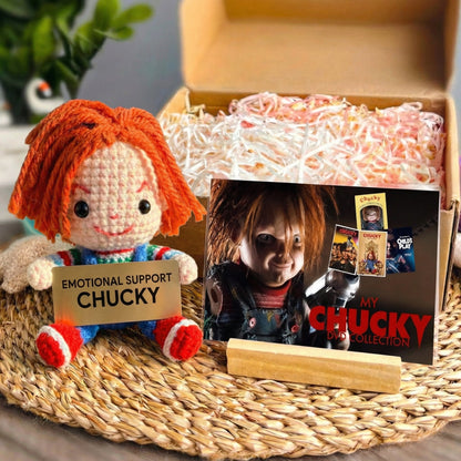 Emotional Support Chucky doll with a box of candy and 'My Chucky Doll Collection' book on a woven surface.