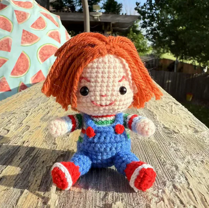 Crocheted doll with orange hair and blue overalls sitting on a wooden surface.