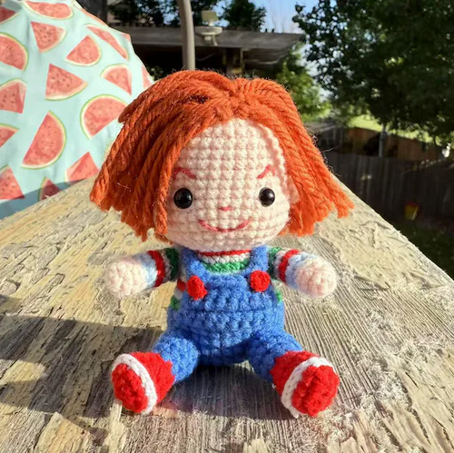Crocheted doll with orange hair and blue overalls sitting on a wooden surface.