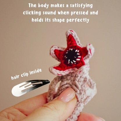 Star-shaped hair clip with red center and white edges, held by a hand against a beige background.